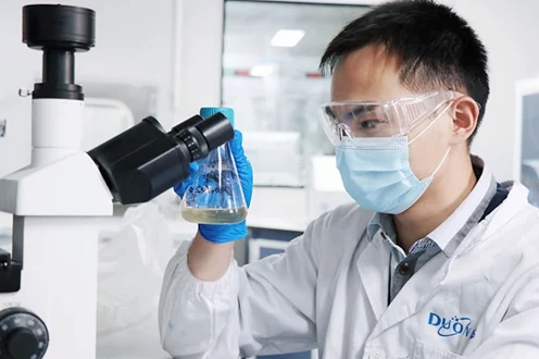 Researcher examining a flask under a microscope